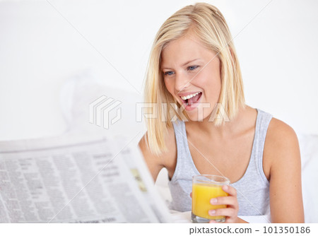 Catching up on her current affairs. A pretty young woman reading the newspaper in bed and enjoying a glass of OJ. 101350186
