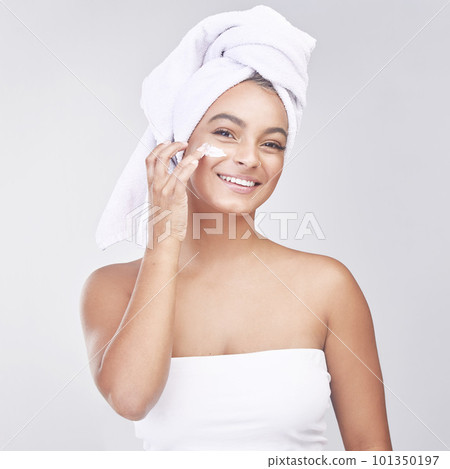 Creating my glow. Studio shot of a beautiful young woman applying moisturiser against a grey background. Creating my glow. Studio shot of a beautiful young woman applying moisturiser against a grey background. 101350197