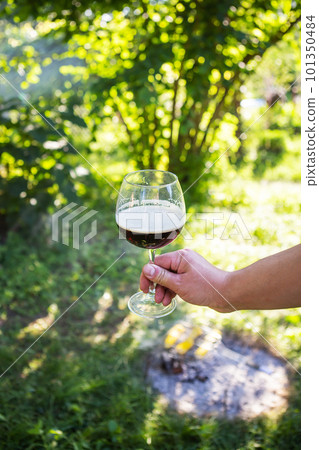 A man holds a glass of beer over a bonfire on a background of green grass. The concept of outdoor recreation, picnic with friends or family. 101350484
