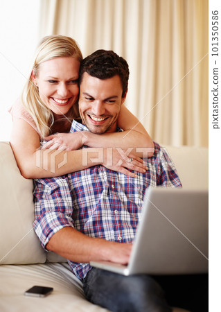 Sharing a funny video clip. A beautiful woman hugging her husband from behind while he sits on the couch working on his laptop. 101350586