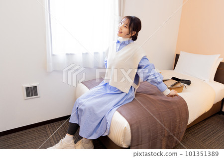 Young woman sitting on bed in room after check-in Young woman sitting on bed in room after check-in 101351389