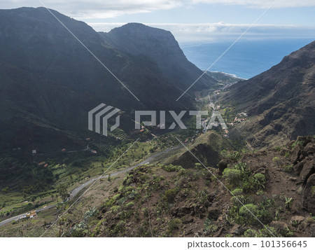 Aerial view from Mirador de Hermigua. Green valley with mountain cliffs, ocean and colorful houses village with terraced fields. La Gomera, Canary island, Spain 101356645