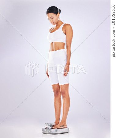 Weightloss, diet and woman weighing on a scale for health, wellness or fitness isolated in a studio white background. BMI, athlete and female measure or checking body mass after exercise or workout 101358516