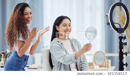 Woman recording a makeup tutorial with a client for her beauty blog or vlog using her phone at home. African American female influencer live streaming her cosmetic skills for social media 101358517