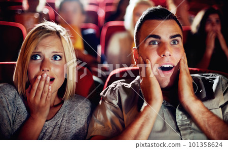 Couple watch a scary, horror or thriller movie in a cinema together and are shocked, wow or surprised. Man and woman in theatre on a date with omgand scared emotion or fear while watching a film 101358624