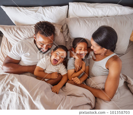 Happy family bonding in bed together, playing and laughing while being loving and having fun. Young caring interracial parents sharing special moment of parenthood with two playful boys in bedroom 101358703