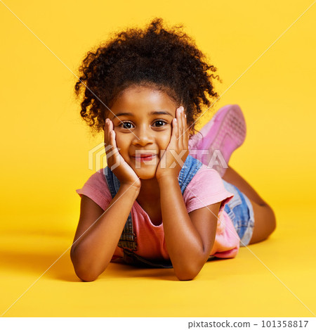 Smile, cute and portrait of a child on the floor isolated on a yellow background in a studio. Adorable, sweet and an innocent girl lying down looking happy, beautiful and relaxed on a backdrop 101358817