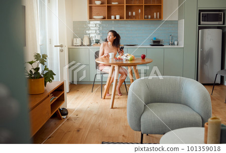 Woman on phone thinking of breakfast idea, healthy snack while drinking coffee in the morning in stylish kitchen. Relaxed and alone girl looking nostalgic in a modern apartment with interior design Woman on phone thinking of breakfast idea, healthy snack while drinking coffee in the morning in stylish kitchen. Relaxed and alone girl looking nostalgic in a modern apartment with interior design 101359018
