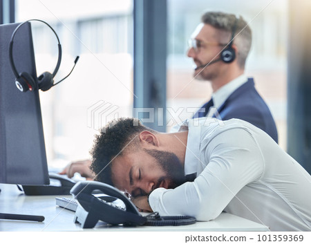 Lazy, sleeping and tired call center agent at his table or desk at work overworked suffering from burnout. Exhausted young customer service employee asleep in the office or workplace 101359369