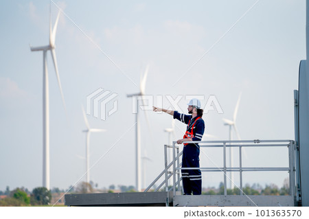 Engineer man or technician worker stand on base of windmill or wind turbine and point to left side Engineer man or technician worker stand on base of windmill or wind turbine and point to left side 101363570