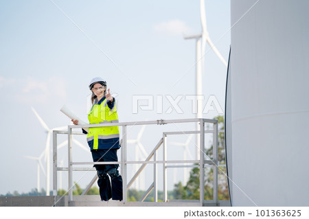 Engineer or technician woman worker hold drawing paper and stand on base of windmill Engineer or technician woman worker hold drawing paper and stand on base of windmill 101363625