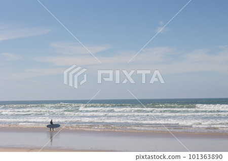 A lone surfer walks along the beach to the sea holding a board 101363890