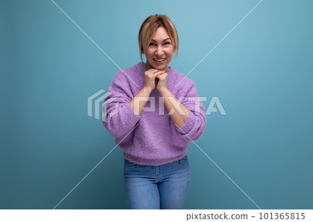 portrait of a modest charming pleasant blond young woman in a purple sweater on a blue background 101365815
