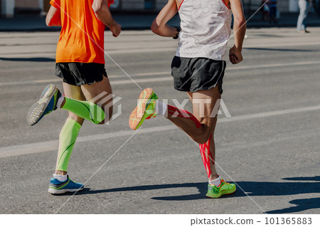 back two athletes runners running marathon in city, legs man jogger in compression sleeves and kinesiotaping calf muscle back two athletes runners running marathon in city, legs man jogger in compression sleeves and kinesiotaping calf muscle 101365883