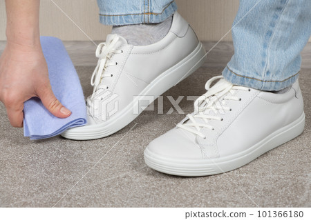 Cleaning white shoes, caring for sneakers. A woman wipes her leather shoes with a wet cloth from dust and dirt. Cleaning white shoes, caring for sneakers. A woman wipes her leather shoes with a wet cloth from dust and dirt. 101366180