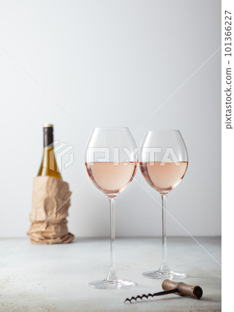 Pink rose glasses of wine with corkscrew and bottle on light board. 101366227