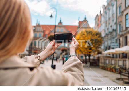 Young adult woman tourist standing with phone making photo or video in old center of Gdansk, Poland. Vacation tourism with app for travel blog Young adult woman tourist standing with phone making photo or video in old center of Gdansk, Poland. Vacation tourism with app for travel blog 101367245