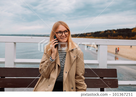 Smiling happy woman having pleasant conversation on mobile phone while sitting near sea during recreation time, young cheerful hipster girl calling with cell telephone while enjoying good day and calm Smiling happy woman having pleasant conversation on mobile phone while sitting near sea during recreation time, young cheerful hipster girl calling with cell telephone while enjoying good day and calm 101367251