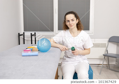 Rehabilitation Specialist, Physical Therapist With Rehab Tools, Foam Roller, Lacrosse Ball, Massage Ball With Pimples, Mesoroller With Titanium Needles, Kinesiology Tape On Couch in Therapeutic Room 101367429