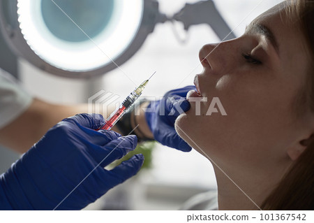 Lip augmentation and correction procedure in a cosmetology salon. The specialist makes an injection in the patient's lips 101367542