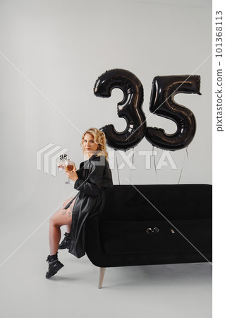 blonde in a black with champagne and cake on the couch. balloons of thirty-five blonde in a black with champagne and cake on the couch. balloons of thirty-five 101368113