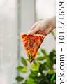 A piece of pizza in his hand, against the backdrop of the restaurant, Side view of the pizza. The concept of Italian cuisine, street food, fast food, fast food. Banner 101371659