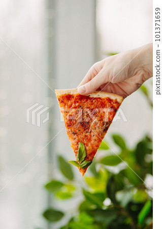 A piece of pizza in his hand, against the backdrop of the restaurant, Side view of the pizza. The concept of Italian cuisine, street food, fast food, fast food. Banner A piece of pizza in his hand, against the backdrop of the restaurant, Side view of the pizza. The concept of Italian cuisine, street food, fast food, fast food. Banner 101371659
