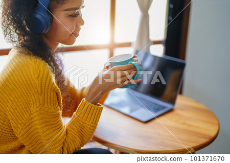 Portrait of an African American wearing headphones holding a coffee cup and using a computer. 101371670