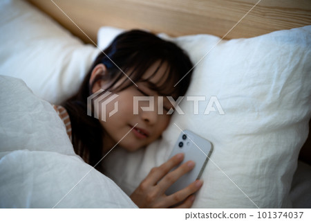 一名年輕女子在使用智能手機時睡著了 101374037