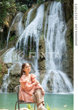 Young Asian woman sitting on a chair In front of the Khoun Moung Keo Waterfall 101375973