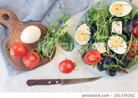 Salad of microgreens, lettuce, tomatoes, cheese and boiled eggs, on a plate, on the table, recipe from natural ingredients, healthy food 101376162