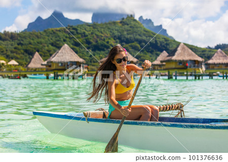 Outrigger Canoe - woman paddling in traditional French Polynesian Outrigger Canoe for recreation sport watersport competition. Bora Bora with Mount Otemanu and overwater bungalow resort hotel. 101376636