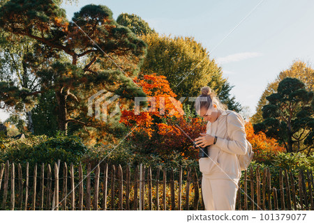 Beautiful young woman takes photos with a professional camera in autumn forest. Smiling girl enjoying autumn weather. Rest, relaxation, lifestyle concept. Young photographer takes pictures of autumn Beautiful young woman takes photos with a professional camera in autumn forest. Smiling girl enjoying autumn weather. Rest, relaxation, lifestyle concept. Young photographer takes pictures of autumn 101379077
