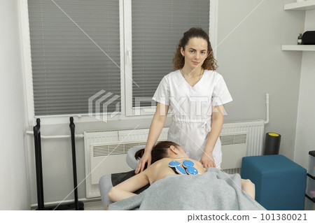 Female Doctor, Physician Sets Wireless Electric Muscle Stimulator On Back Of Disabled Child With Cerebral Palsy. Massage, Rehabilitation. Children with disability, special needs. Horizontal plane 101380021
