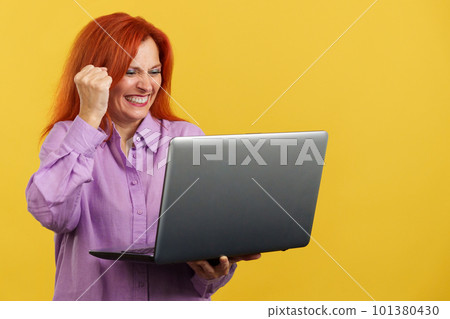 Mature redheaded woman celebrating while looking at the laptop 101380430