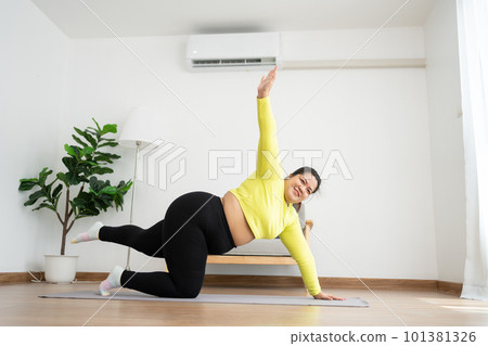Asian overweight woman doing stretching exercise at home on fitness mat. Home activity training, online fitness class. Stretching training workout on yoga mat at home for good health and body shape. Asian overweight woman doing stretching exercise at home on fitness mat. Home activity training, online fitness class. Stretching training workout on yoga mat at home for good health and body shape. 101381326