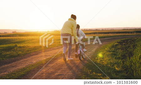 mother rides child bicycle sunset. happy family park. Mom teaches her daughter ride bike. concept happy family summer park. fun vacation. teamwork. mother runs green grass rolling child bicycle mother rides child bicycle sunset. happy family park. Mom teaches her daughter ride bike. concept happy family summer park. fun vacation. teamwork. mother runs green grass rolling child bicycle 101381600