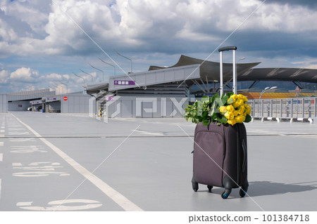 A suitcase and a bouquet of yellow roses in the airport parking lot. Summer vacation concept A suitcase and a bouquet of yellow roses in the airport parking lot. Summer vacation concept 101384718