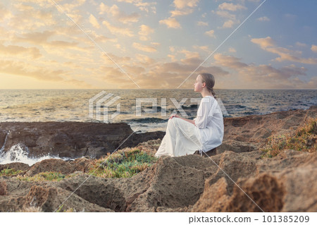 Teenage girl sitting on rocks near blue sea 101385209