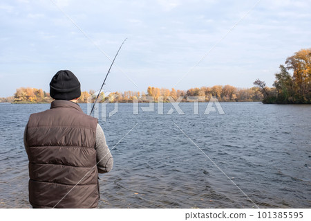 A fisherman stands on the bank of the river with a spinning rod in his hands and catches fish. 101385595