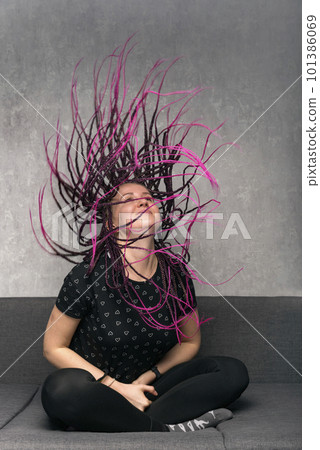 Happy woman waves her dreads with long violet dreadlocks sitting on sofa. Vertical frame. Stylish girl 101386069