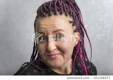 Close up portrait of middle-aged woman with pink dreadlocks writhing grimace. Emotion of surprise and smirk. 101386071