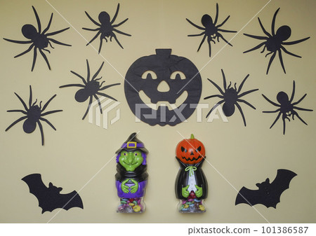 Scary Halloween figurines stand on a light background in close-up, behind hangs terrible pumpkin, spiders and bats Scary Halloween figurines stand on a light background in close-up, behind hangs terrible pumpkin, spiders and bats 101386587