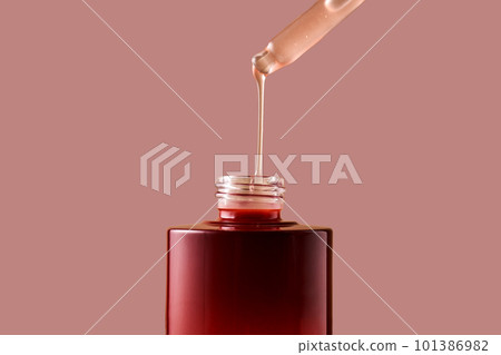 A drop of pink cosmetic drips from the dropper into a burgundy bottle. A drop of pink cosmetic drips from the dropper into a burgundy bottle. 101386982
