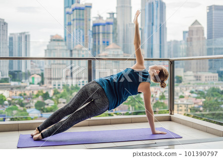 Young woman is practicing yoga in the morning on her balcony with a panoramic view of the city and skyscrapers Young woman is practicing yoga in the morning on her balcony with a panoramic view of the city and skyscrapers 101390797