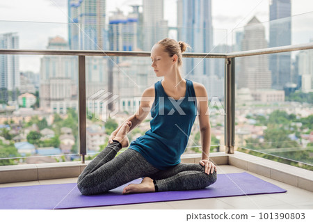 Young woman is practicing yoga in the morning on her balcony with a panoramic view of the city and skyscrapers 101390803
