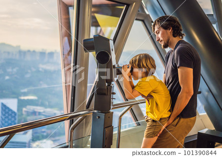 Dad and son are looking at Kuala lumpur cityscape. Use binoculars. Panoramic view of Kuala Lumpur city skyline evening at sunset skyscrapers building in Malaysia. Traveling with kids concept 101390844