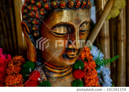 Close up of bronze buddha statue sitting in meditation with flower decorations for festival ceremony. Close up of bronze buddha statue sitting in meditation with flower decorations for festival ceremony. 101391159