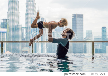 Father and son in outdoor swimming pool with city view in blue sky Father and son in outdoor swimming pool with city view in blue sky 101391271