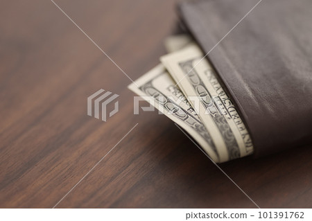 Bespoke brown all leather wallet on walnut table with us dollar cash 101391762